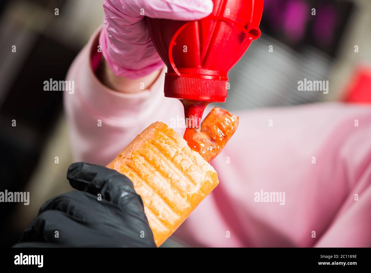 bartender adding ketchup sauce in french hot dog with grill sausage