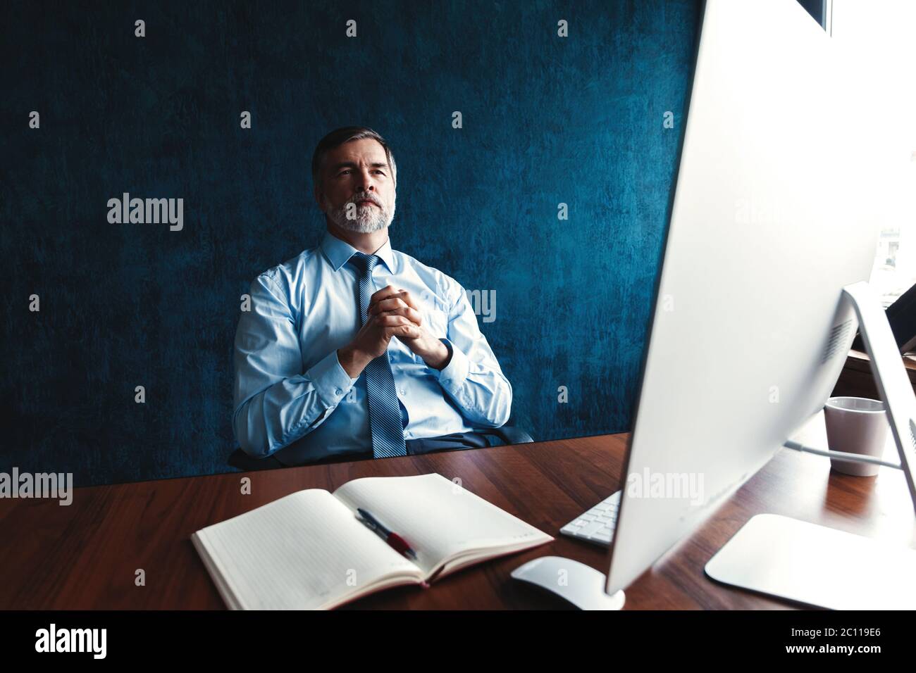 Focused mature businessman deep in thought while sitting at a table in modern office. Stock Photo