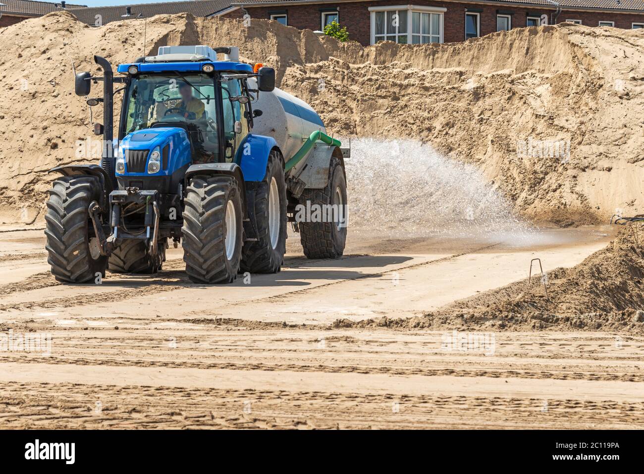 tractor with water tank spread water over a sandy area Stock Photo