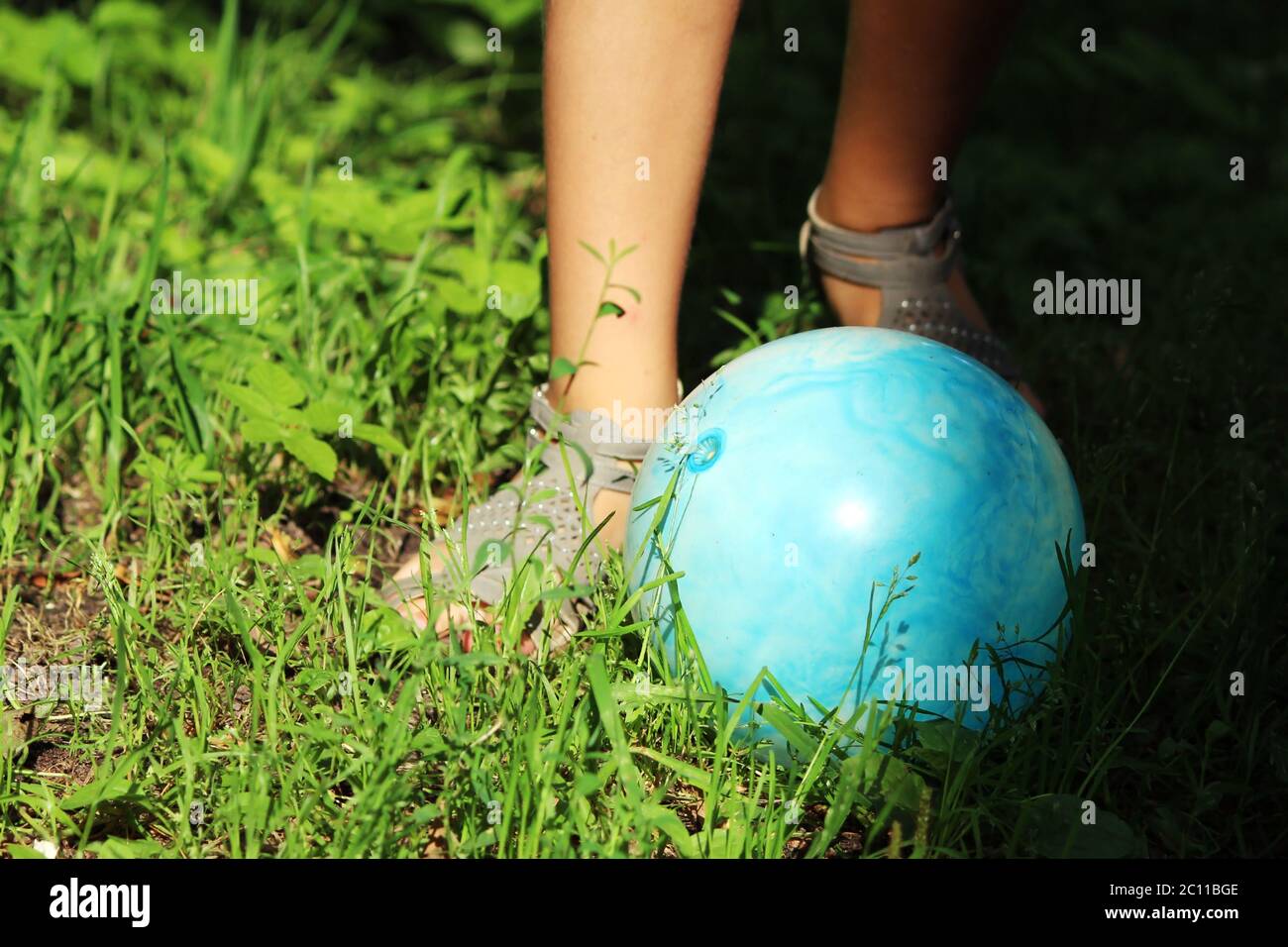 teen girl in sandals kicking a blue ball in the park on the grass. Stock Photo