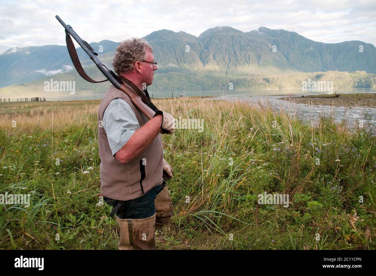 A hunter holding a shotgun and wearing fishing waders in a creek estuary in the Great Bear Rainforest, near Bella Coola, British Columbia, Canada. Stock Photo