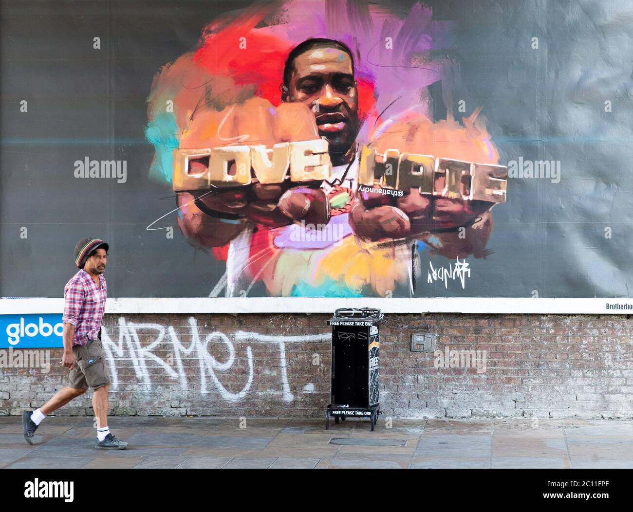 London, UK. 13th June, 2020. People in Shepherd's Bush walk past a large poster with a picture of George Floyd wearing a ring with the words 'Love' and 'Hate'. George Floyd died on May 25th after a police officer applied pressure to his neck, stopping him breathing. Credit: Tommy London/Alamy Live News Stock Photo