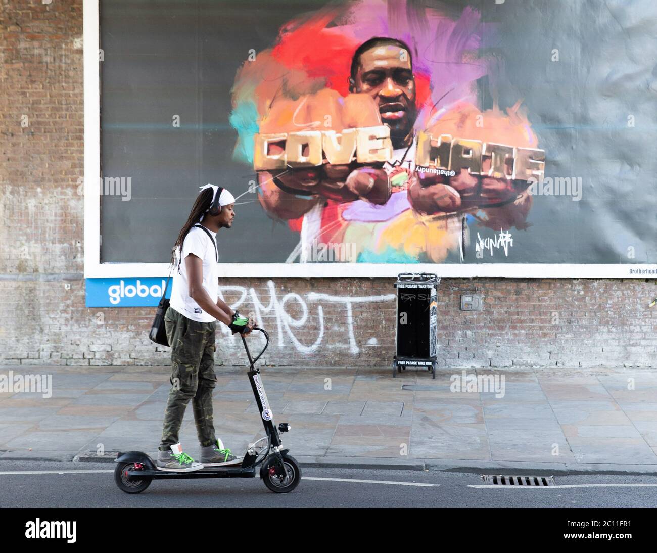 London, UK. 13th June, 2020. People in Shepherd's Bush walk past a large poster with a picture of George Floyd wearing a ring with the words 'Love' and 'Hate'. George Floyd died on May 25th after a police officer applied pressure to his neck, stopping him breathing. Credit: Tommy London/Alamy Live News Stock Photo