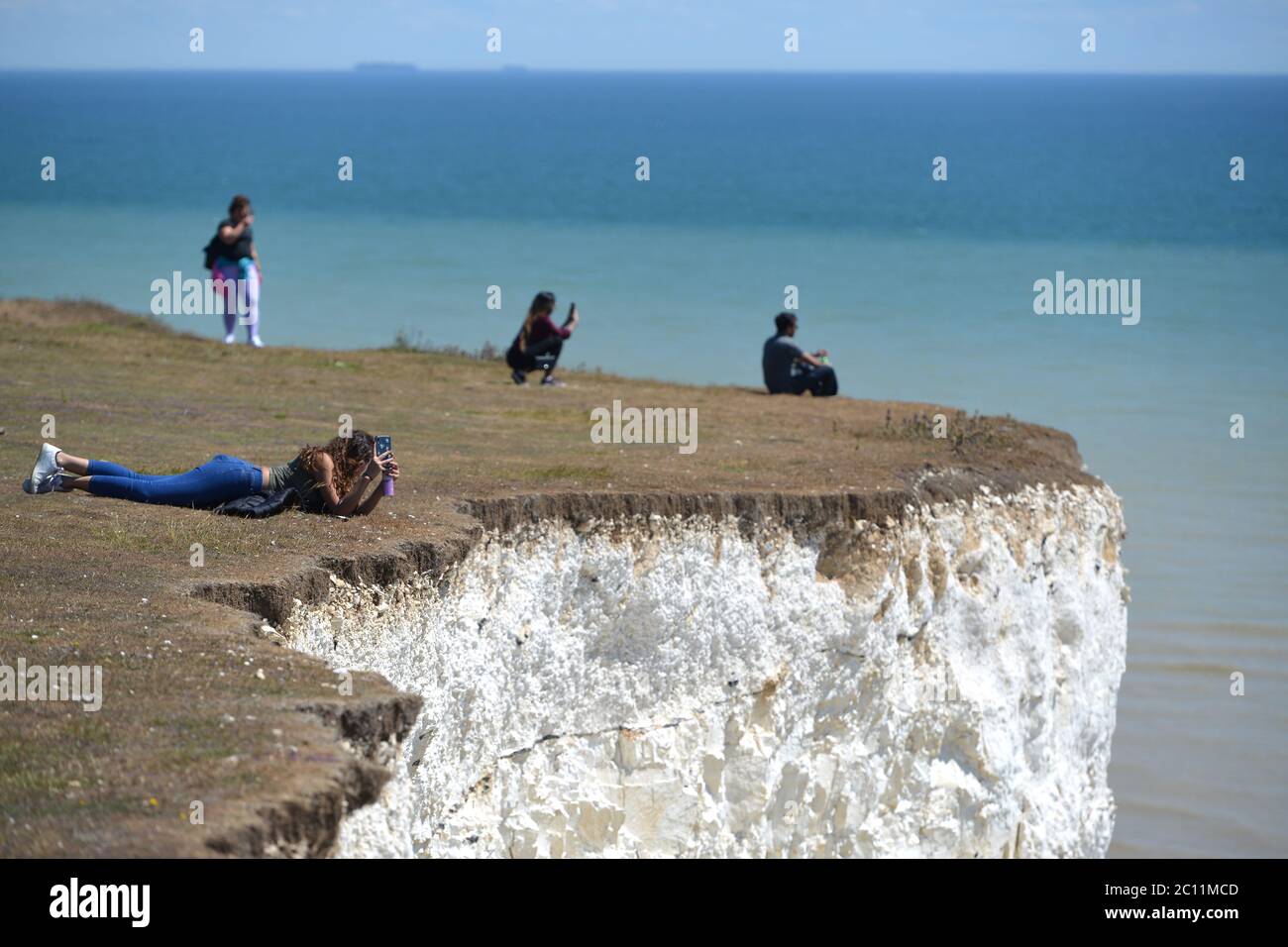 Birling Gap, East Sussex, UK. 13th June, 2020. Tourists get too close to the edge of the crumbling Seven Sisters white chalk cliffs on the Sussex Coast. The iconic cliffs tower up to 400ft above the English Channel. Credit: Peter Cripps/Alamy Live News Stock Photo