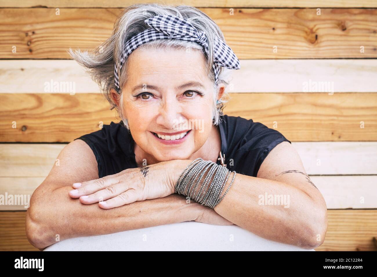 Portrait of cheerful caucasian senior happy woman with wood background - alternative and young old female smile and enjoy - tatooed skin for diversity Stock Photo