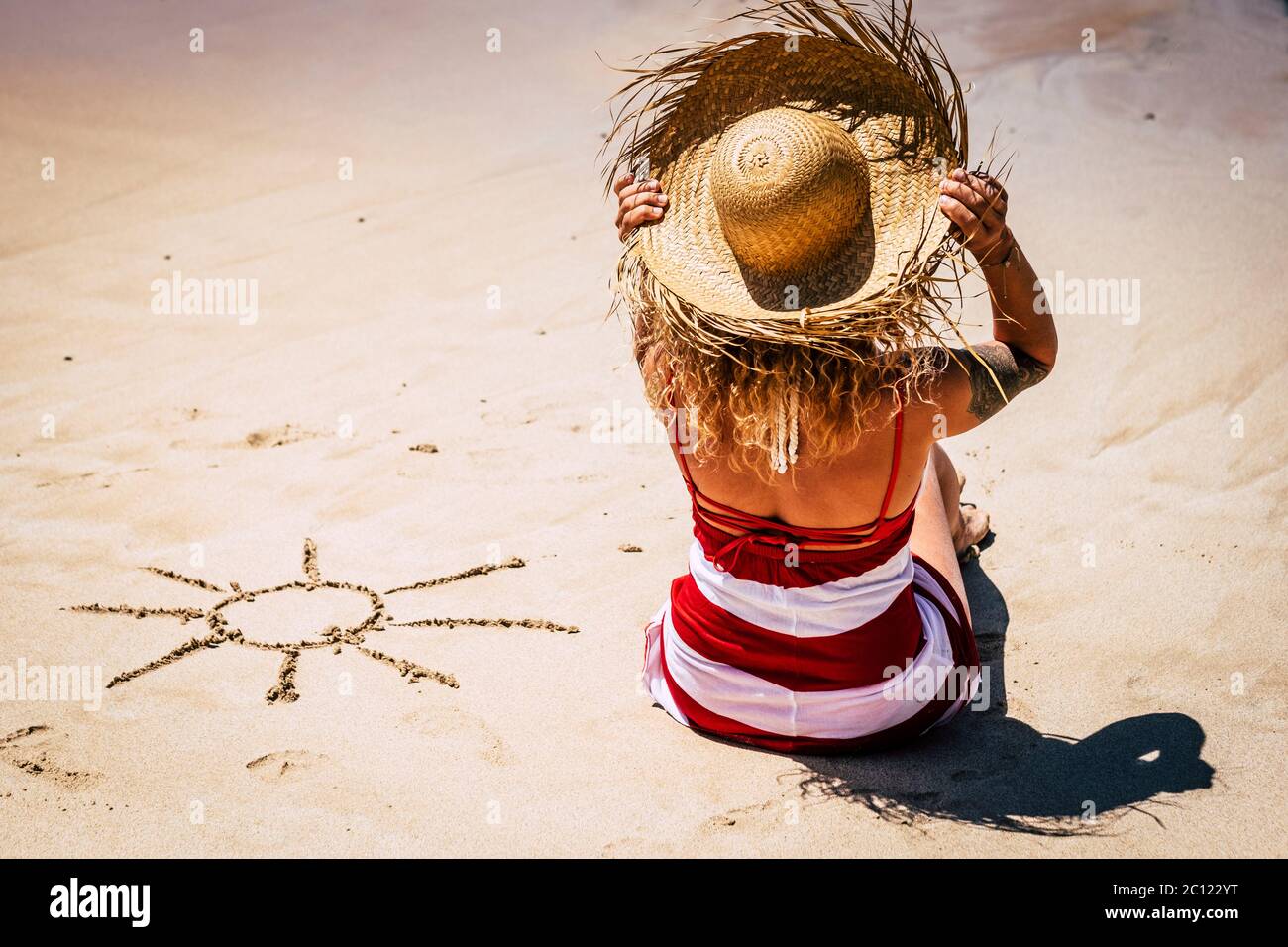Sun and summer holiday vacation concept with people at the beach and caucasian woman viewed from back with tourist hat enjoying the day and the outdoo Stock Photo