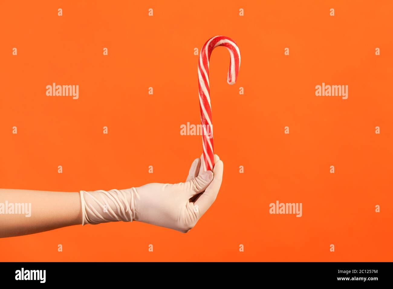 Profile side view closeup of human hand in white surgical gloves holding and showing Christmas stripped red and white candy cane . indoor, studio shot Stock Photo