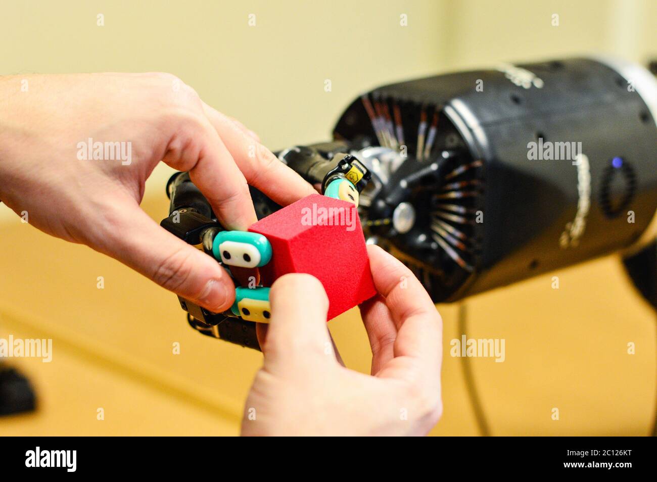 Man Lets Robot Hand Holding a Red Cube in Research Laboratory. Stock Photo