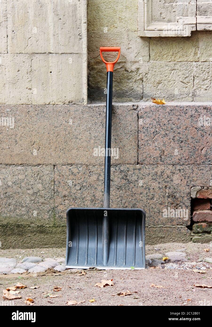 New black shovel with orange handle is leaning against the wall of the palace waiting for clearance from the alley  fallen leave Stock Photo
