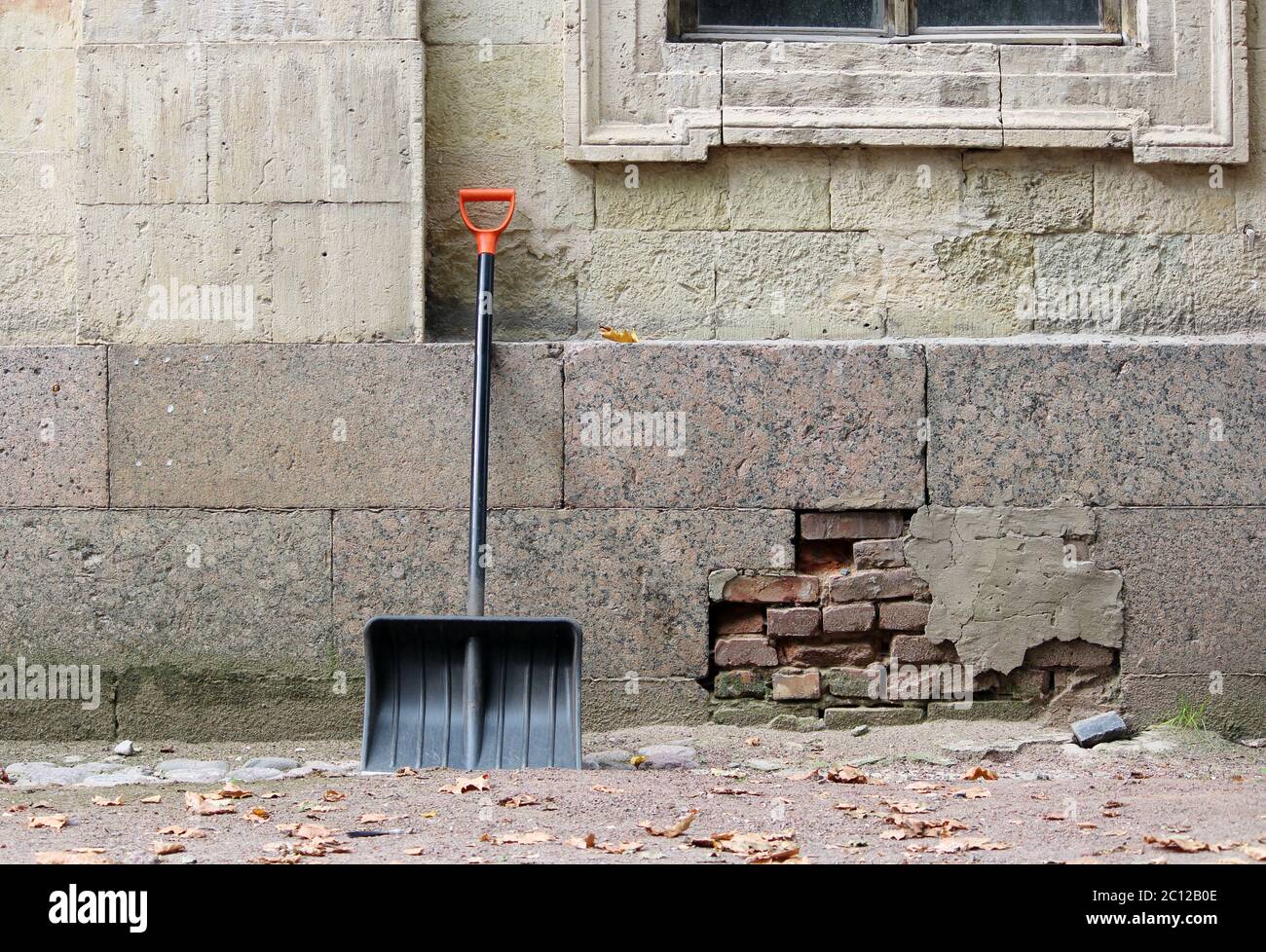 New black shovel with orange handle is leaning against the wall of the palace waiting for clearance from the alley  fallen leave Stock Photo