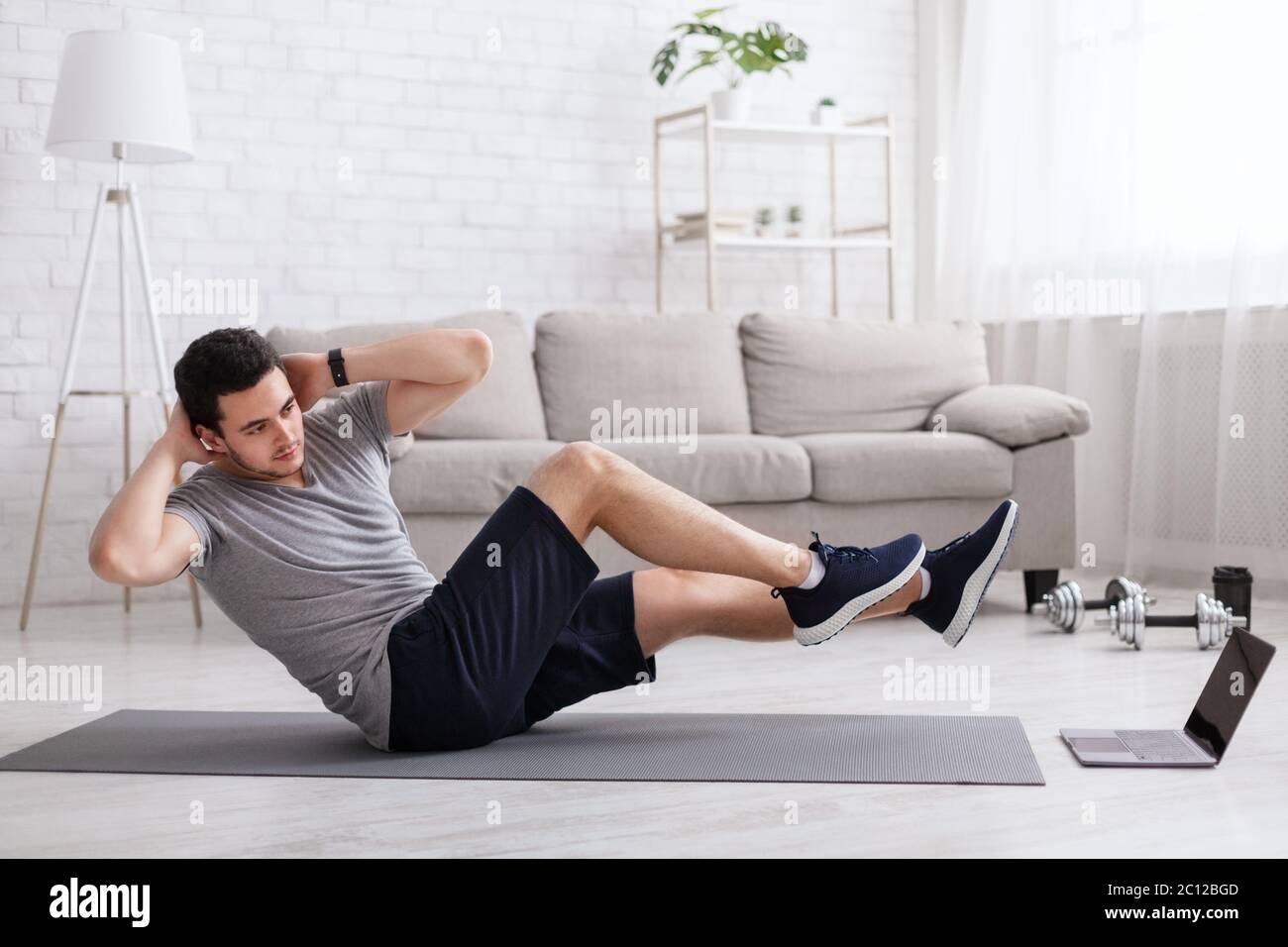 Sport and healthy lifestyle. Man does exercises for abdominal muscles and watches online training Stock Photo
