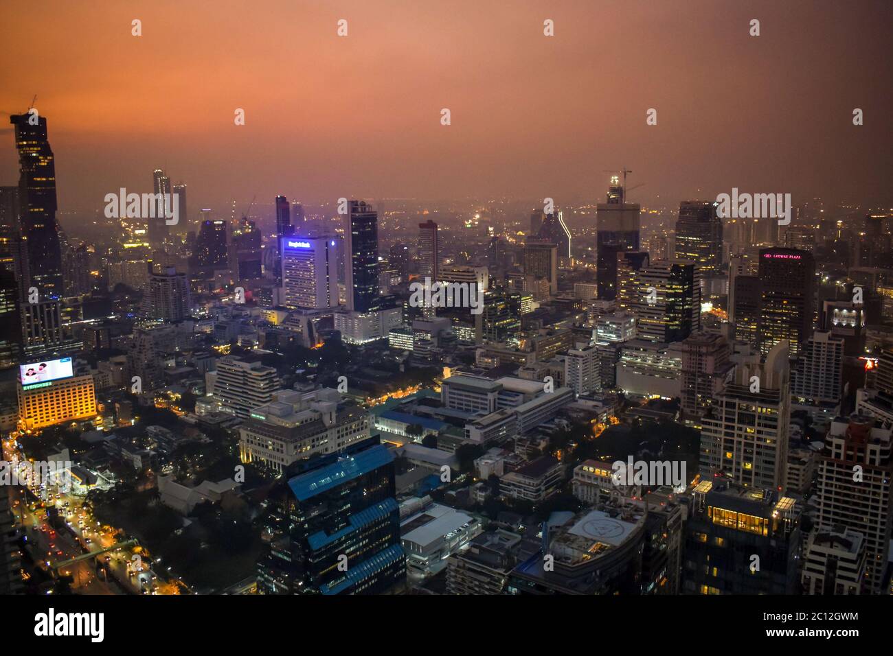 The enlightened skyscrapers of Bangkok skyline during smoggy orange sunset in Thailand Stock Photo