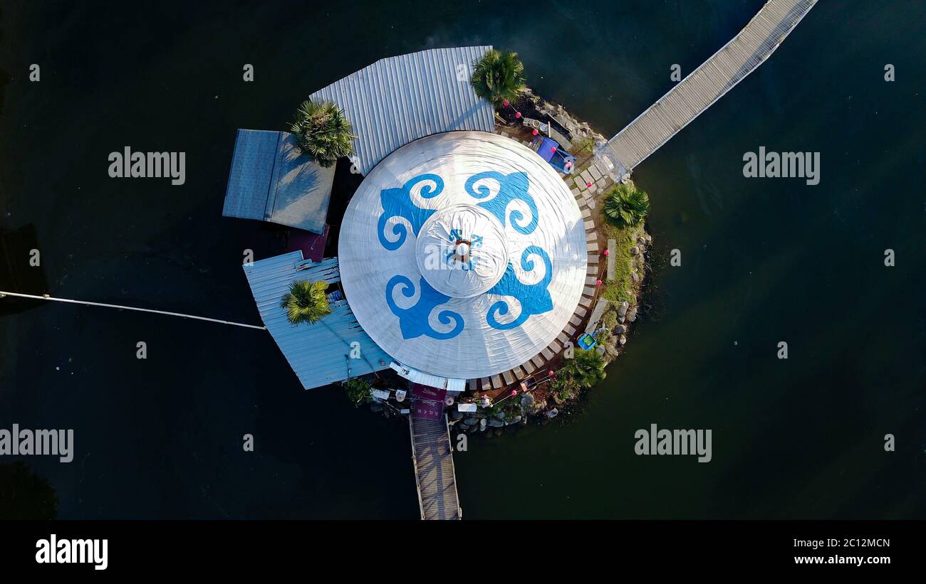 Aerial view on Mongolian white styled Yurt with blue ornaments in the middle of a small water reservoir with two bridges. Stock Photo