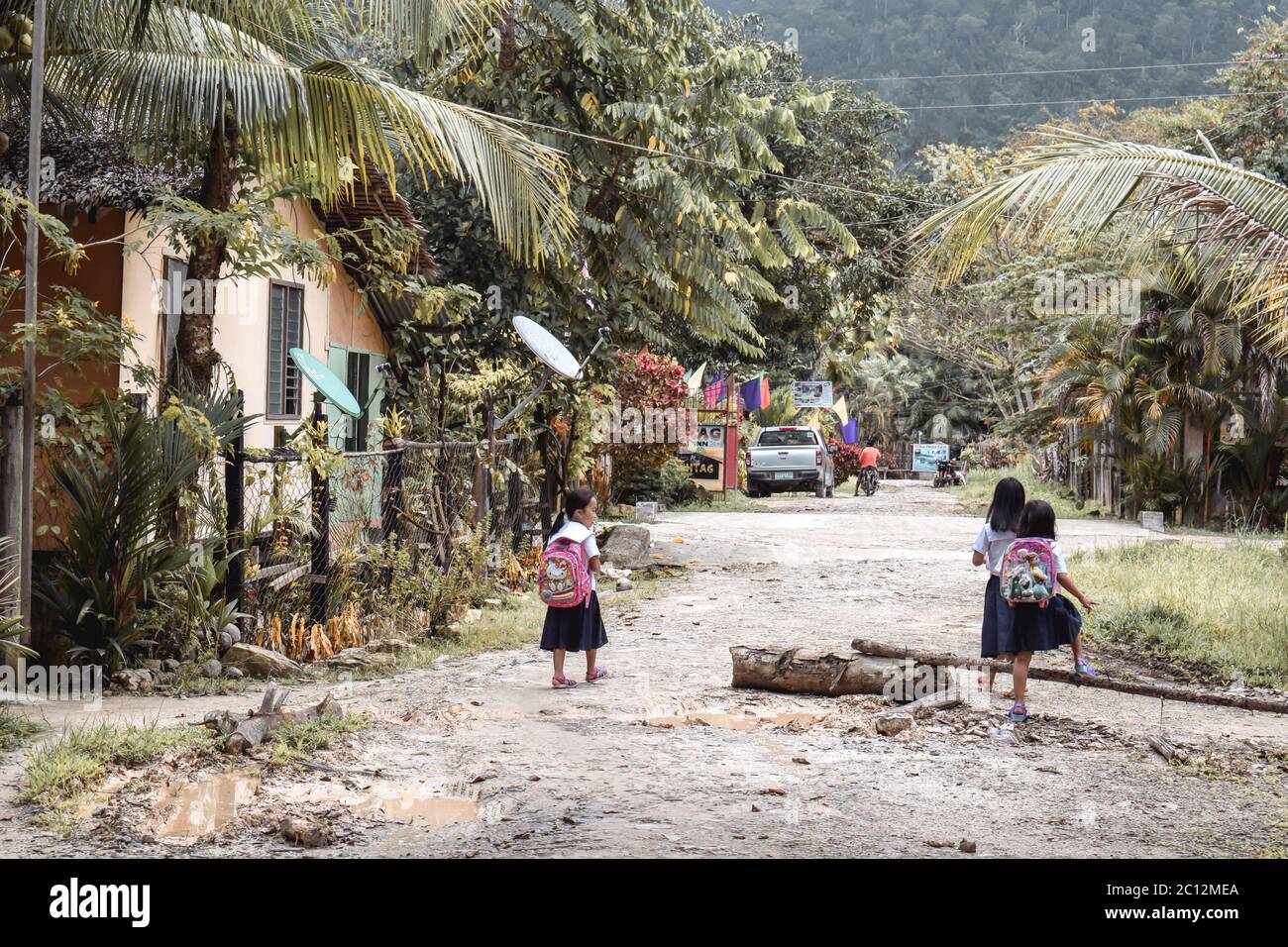 Little Asian school girls walking to school on a muddy road in a jungle conditions in Port Barton Palawan the Philippines Stock Photo