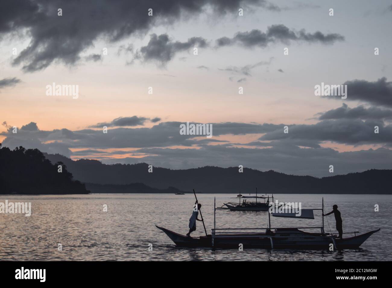Philippine Fisherman fishing on a traditional boat during a beautiful sunset in a lagoon of Port Barton at Palawan island in the Philippines Stock Photo