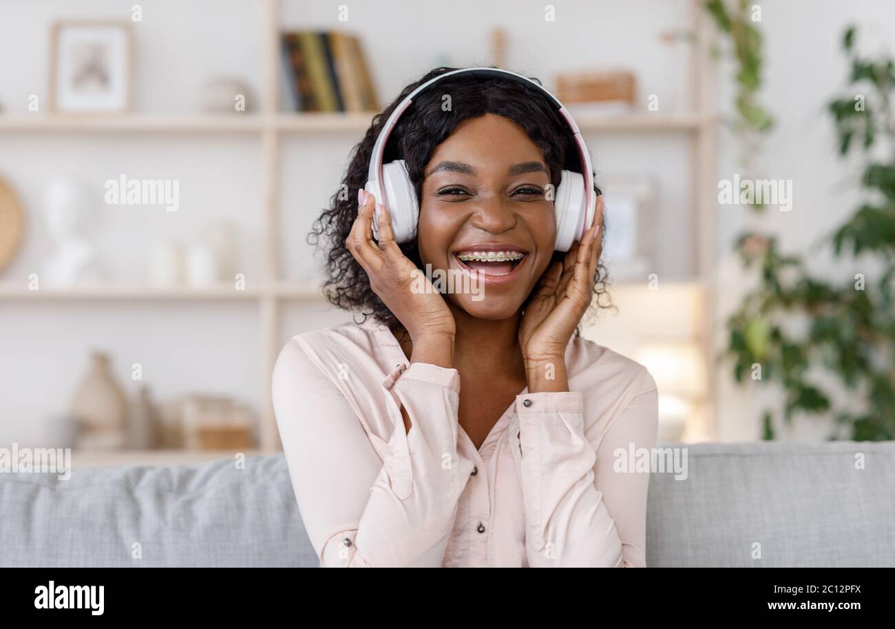 Joyful black girl with braces listening music in wireless headphones at ...