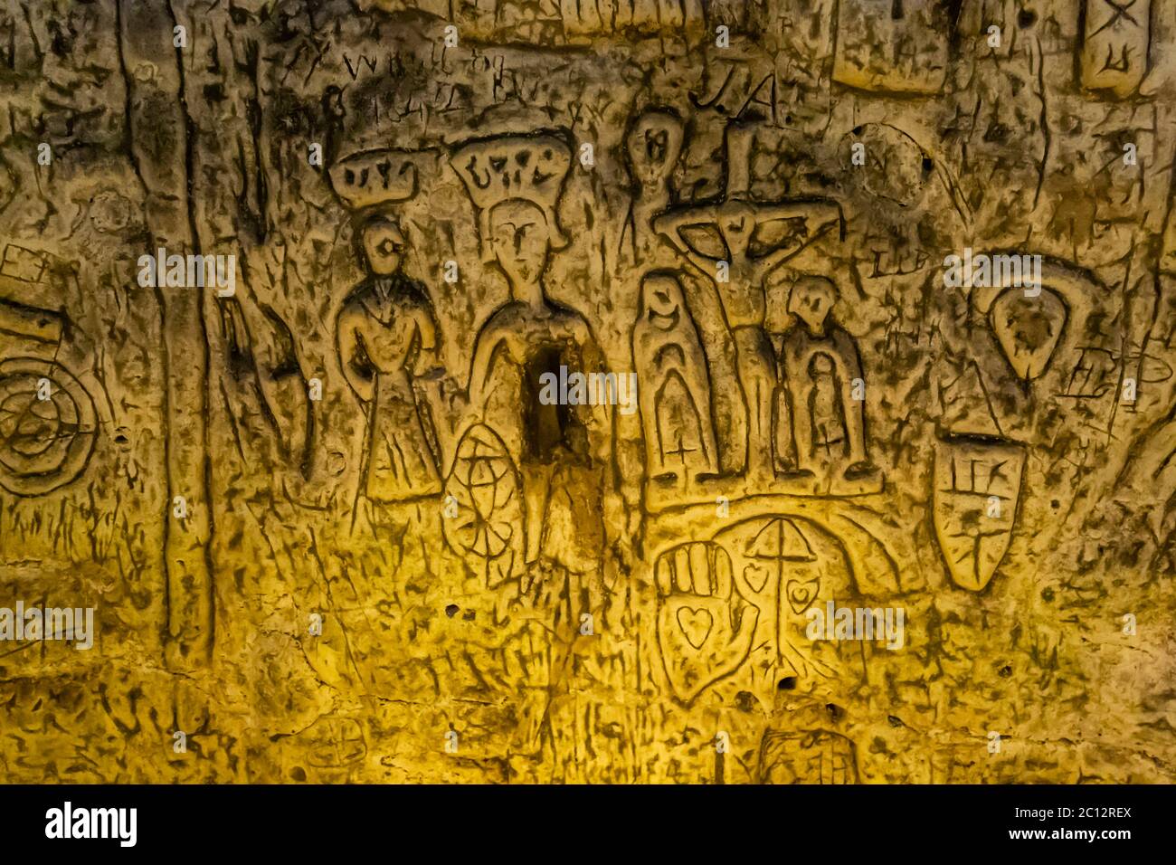 Royston Cave is decorated with a variety of low-relief wall sculptures. They are mainly Christian motifs in the medieval style. Here is a crucifixion scene. The two figures below St Katherine could be King Richard I, known as King Lionheart and his wife Berengaria whose crown is shown floating above her head as she was never actually crowned Queen. Below the crucifixion a palm with an engraved heart. Royston Cave in Katherine's Yard, Melbourn Street, Royston, England Stock Photo