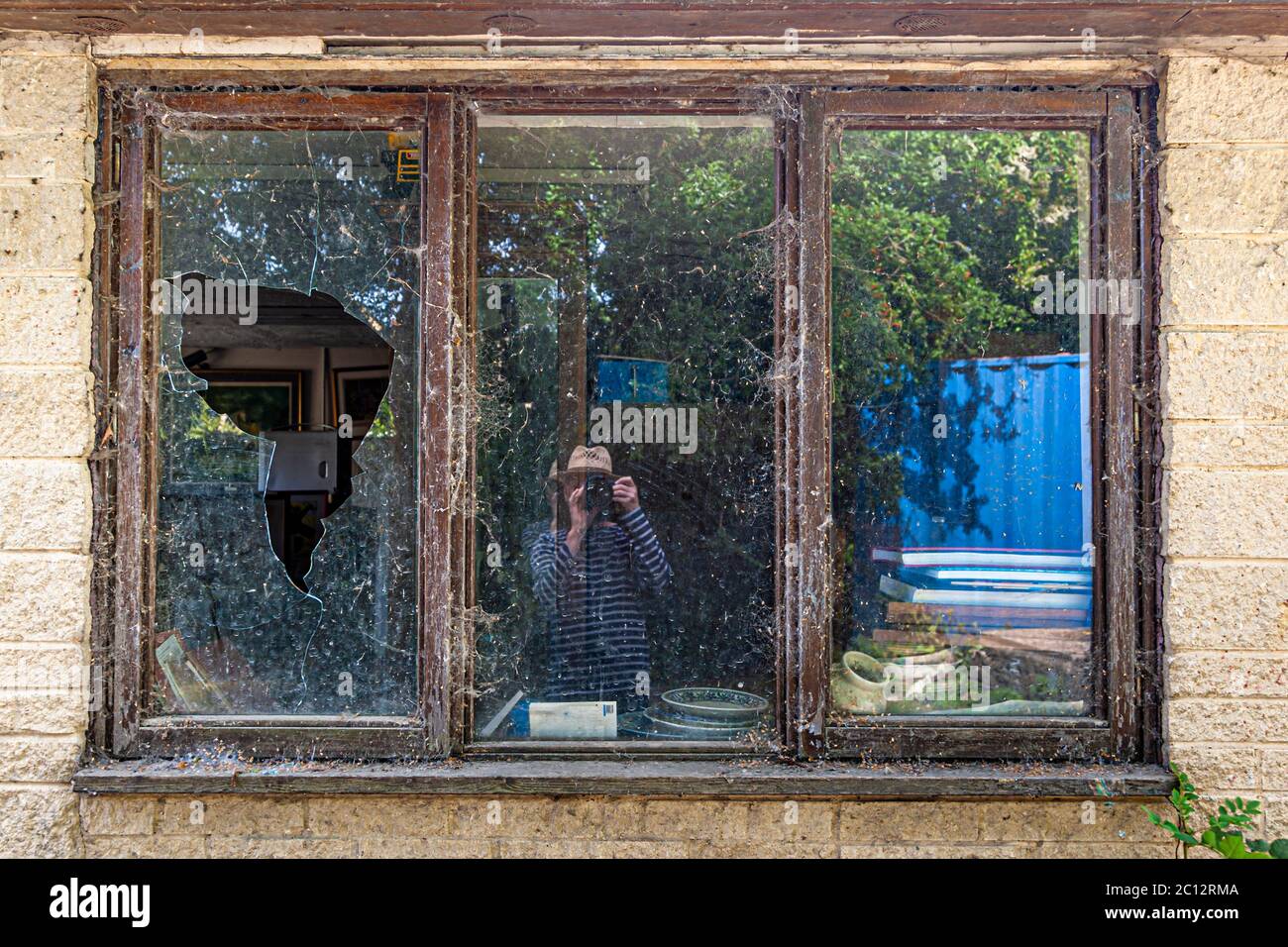 A photographer reflected in the broken window of an abandoned house Stock Photo