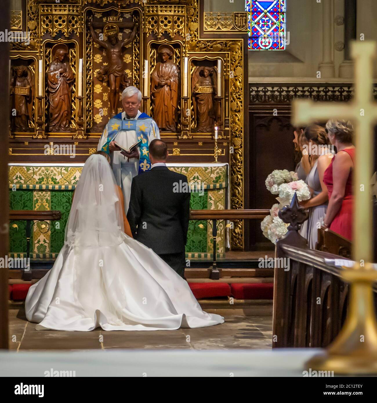 The wedding couple kneels at the altar in front of the Anglican vicar. British Wedding in South Cambridgeshire, England Stock Photo