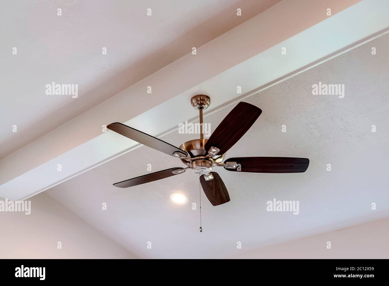 Decorative wood beam with standard ceiling fan and lights inside a house Stock Photo