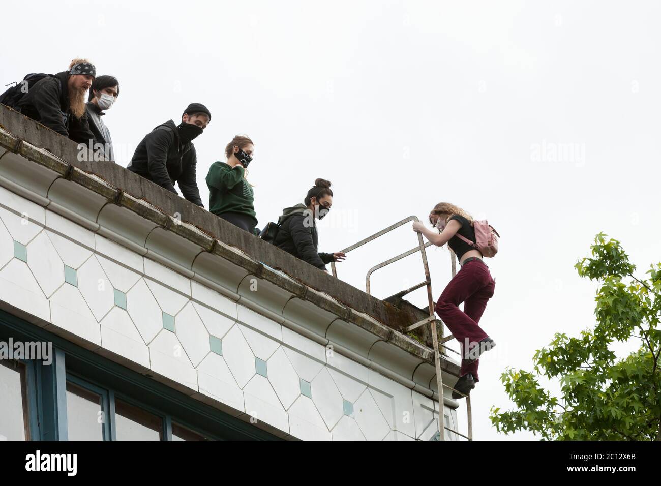 A young woman climbs the fire escape of the Kelly-Springfield Motor Truck Building to access the roof in the “Capitol Hill Autonomous Zone” in Seattle on Friday, June 12, 2020. The zone, also known as CHAZ, is a self-declared intentional community and commune established when the Seattle Police Department closed the East Precinct after days of large protests and occasional violent clashes. Stock Photo