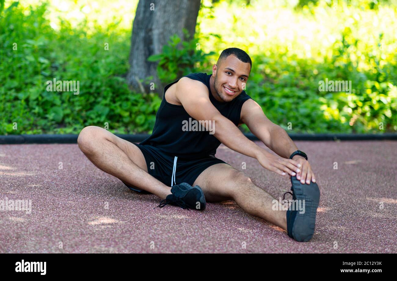 Handsome African American athlete stretching on jogging track in park Stock Photo