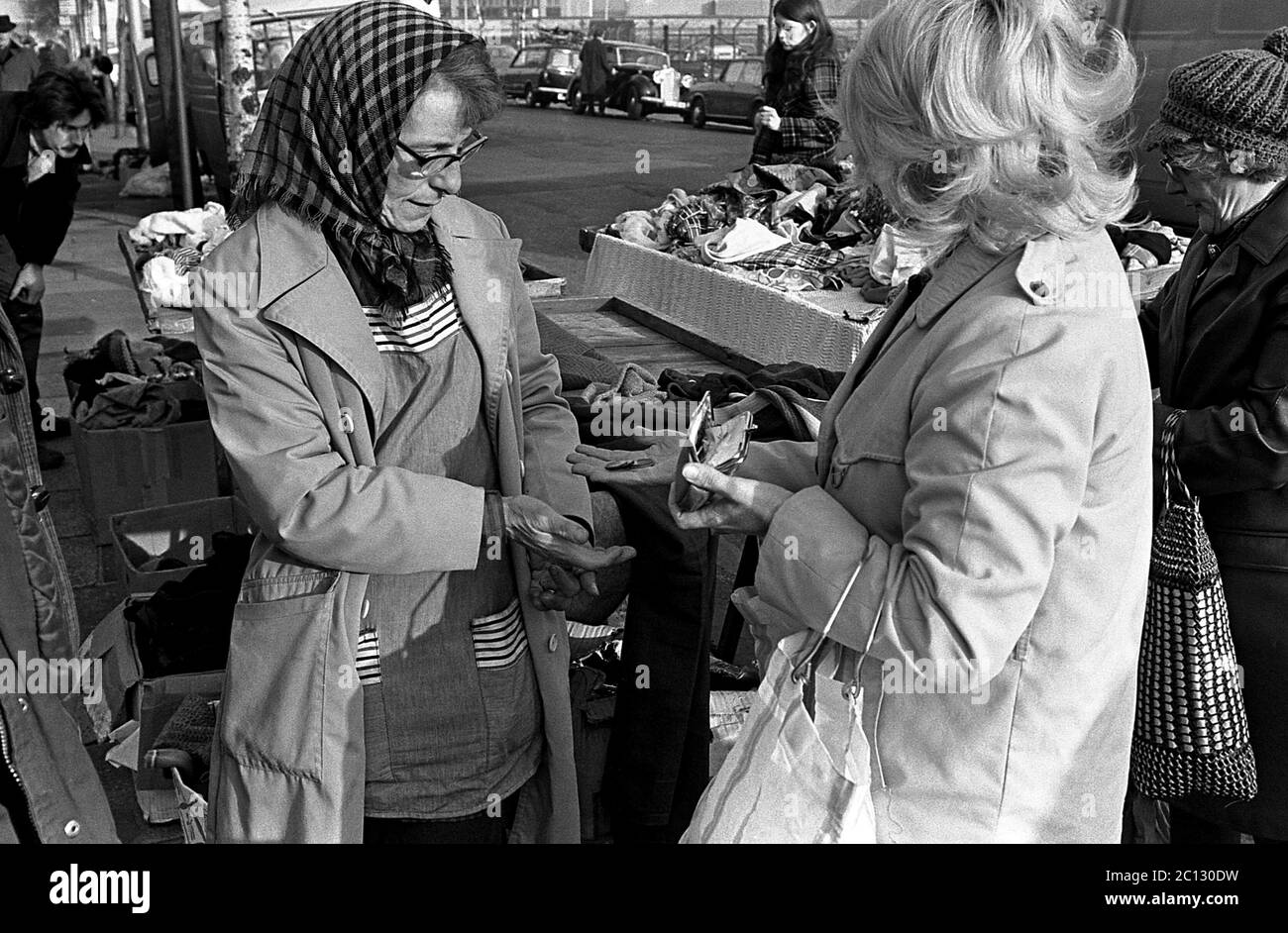 AJAXNETPHOTO. 27TH FEBRUARY, 1975. PORTSMOUTH, ENGLAND. - FLEA MARKET - IN UNICORN ROAD; A BUYER HANDS OVER A FEW COINS TO STREET TRADER (LEFT).PHOTO:JONATHAN EASTLAND/AJAX REF:7513 25A 110 Stock Photo