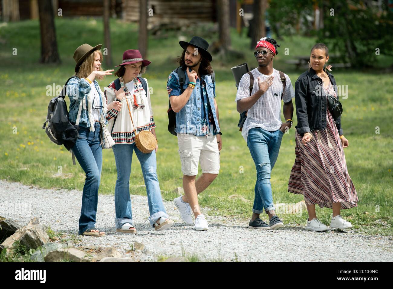 Group of young multi-ethnic friends walking path together and talking while enjoying weekends at festival campsite Stock Photo