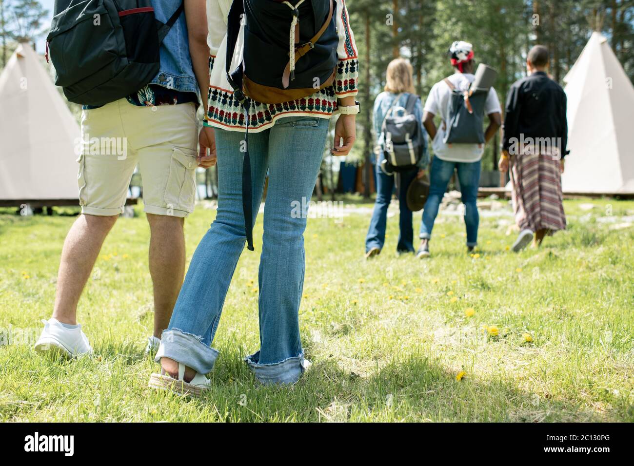 Close-up of people with satchels standing on grass and choosing tents at festival campsite Stock Photo