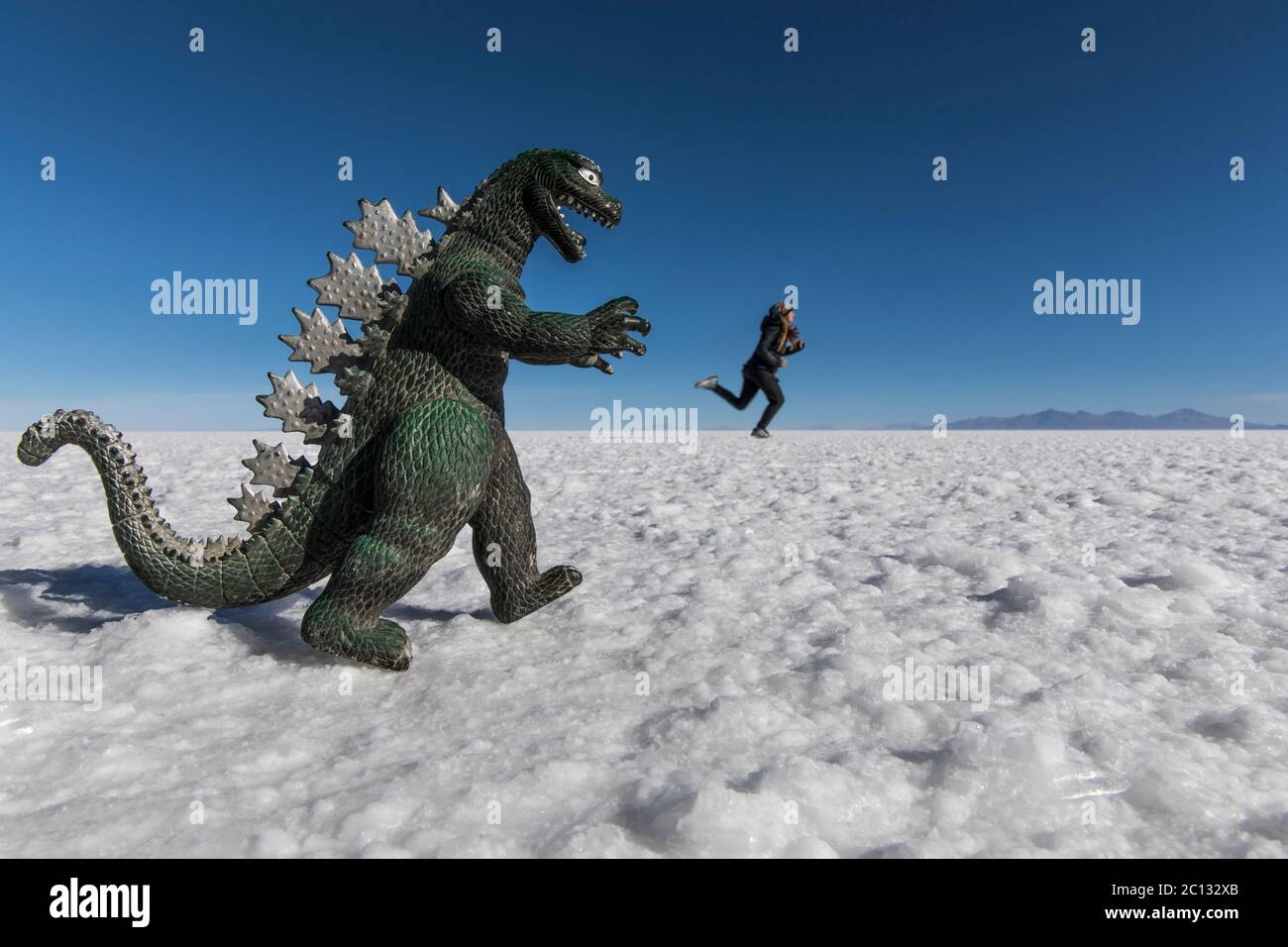 woman playing with perspective in salt flats escaping from a dinosaur Stock Photo