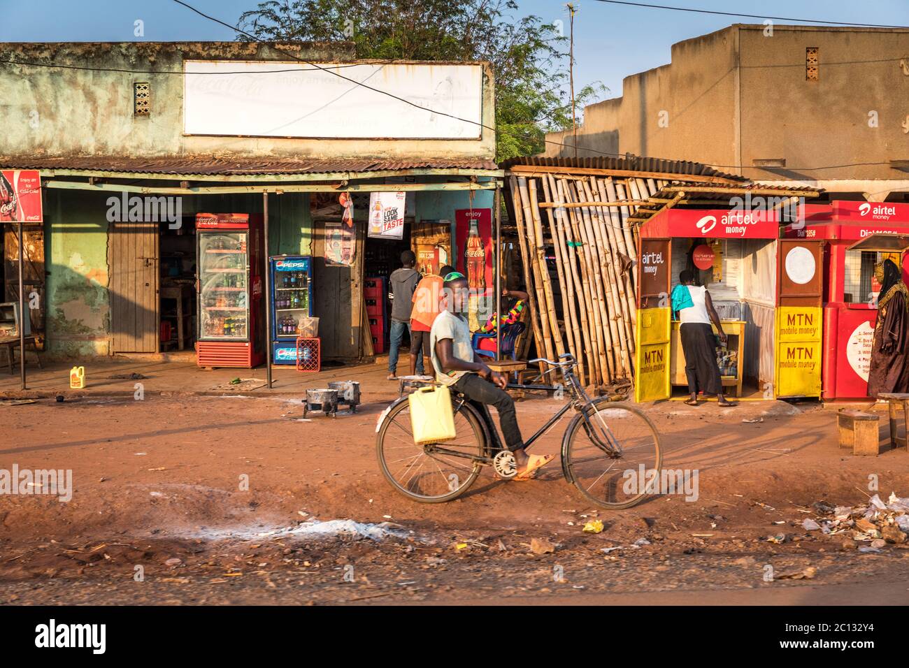 Roadside shops in rural Ugandan village with children in the street and a red dirt road, Uganda, Africa Stock Photo
