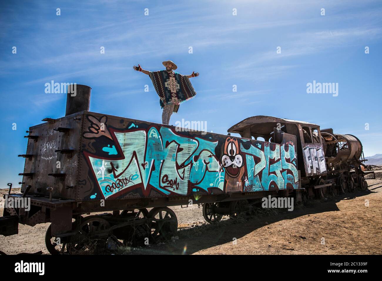 man standing on top of an abandoned train in a train cemetery with a beautiful blue sky in the background Stock Photo