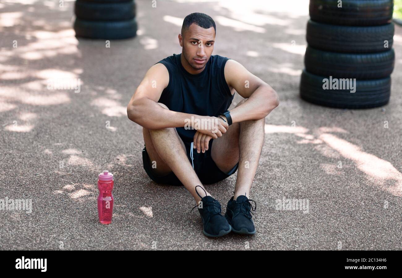 Handsome black man sitting on jogging track at park, resting after his training Stock Photo