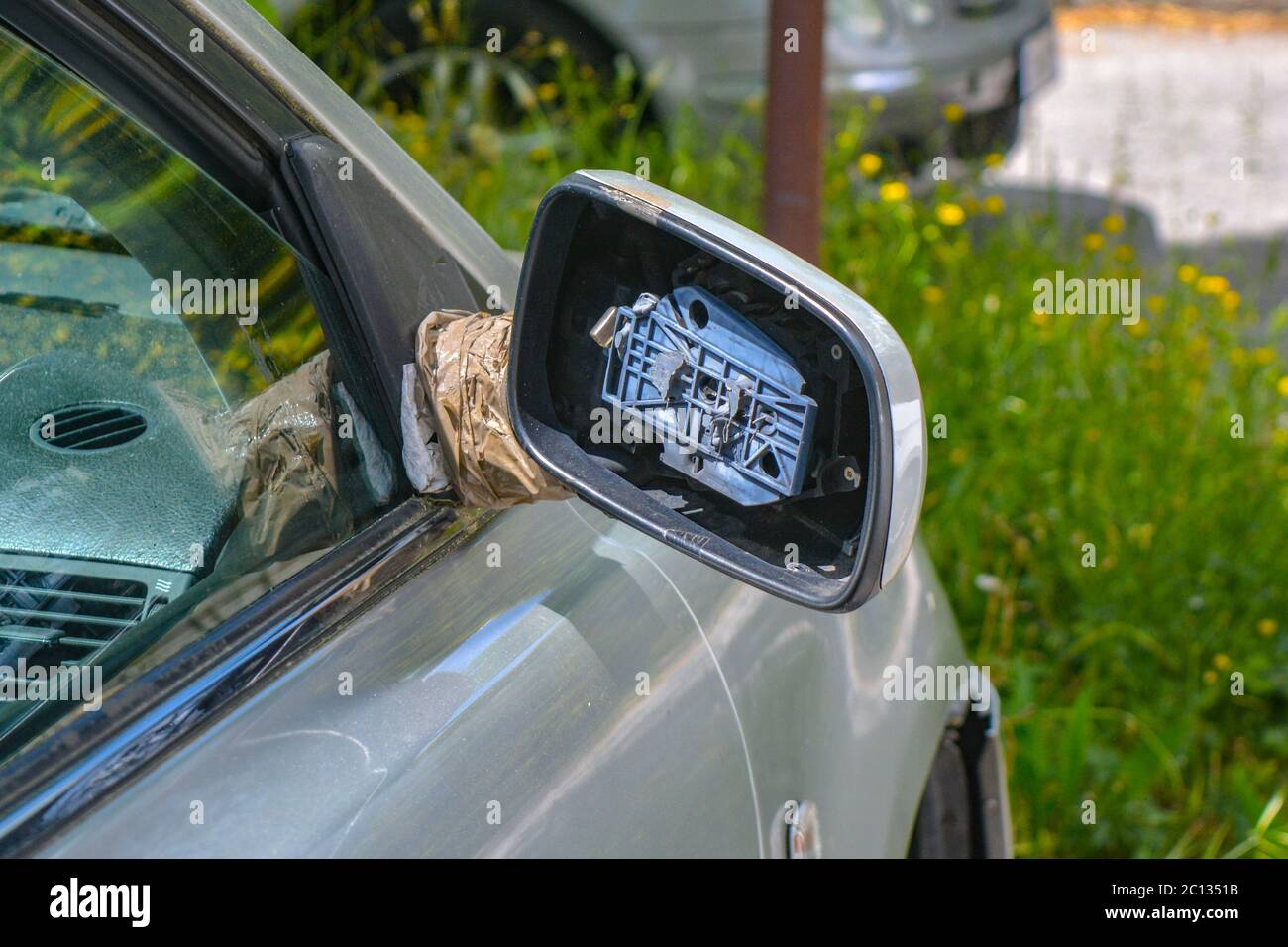 A shattered, broken car rearview mirror after accident. Side view mirror of a silver car has been badly damaged as result of vandalism. Auto part Stock Photo