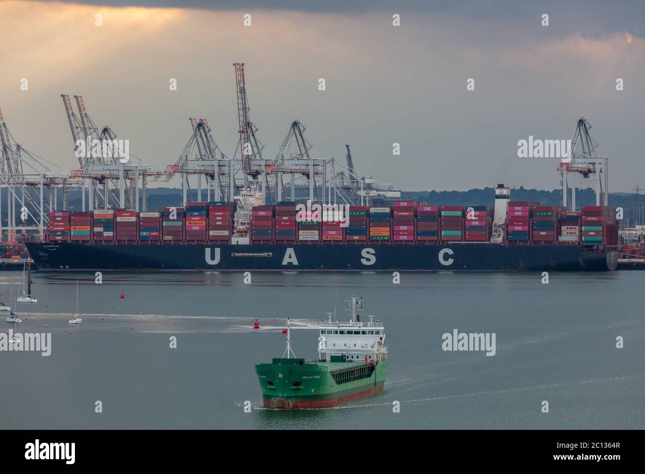 Aerial view of Southampton port. Sunset. Massive container ship 'UASC' being loaded in the background. 'Arklow Rogue' ship sailing in the foreground. Stock Photo