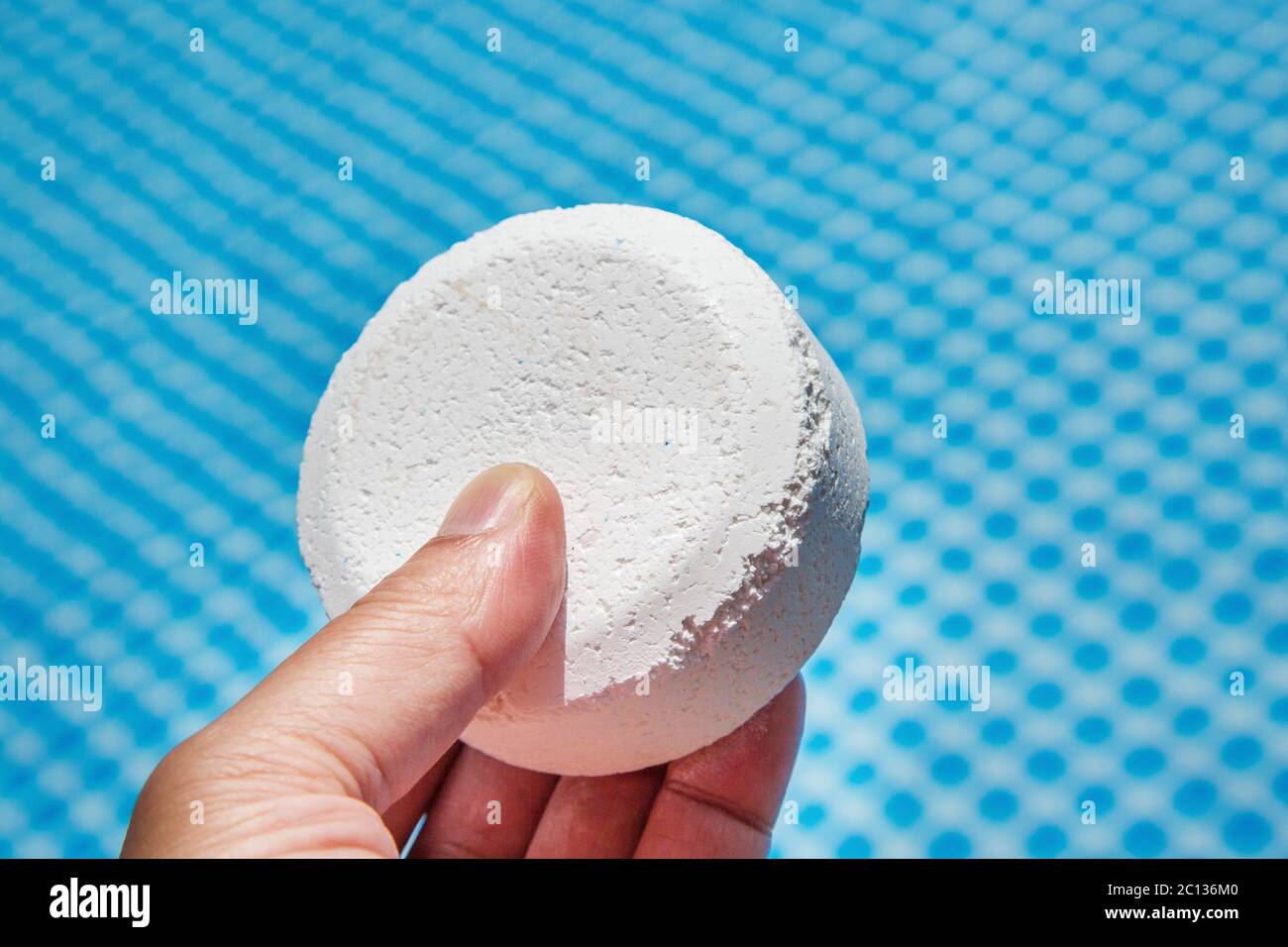 Hand holding Chlorine Pellets with inflatable pool on background Stock Photo