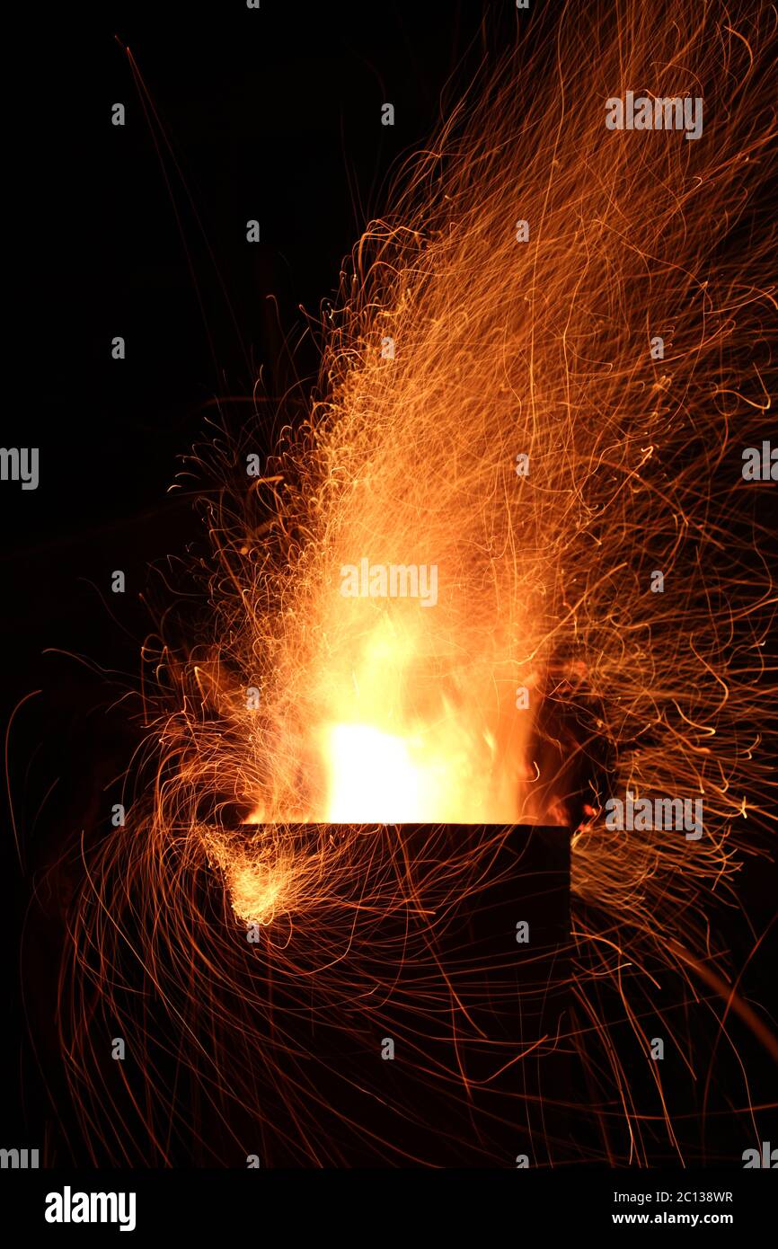 Flames of fire and sparks from firewood burning in a metal outside fireplace at night against a dark sky. Slow shutter speed Stock Photo