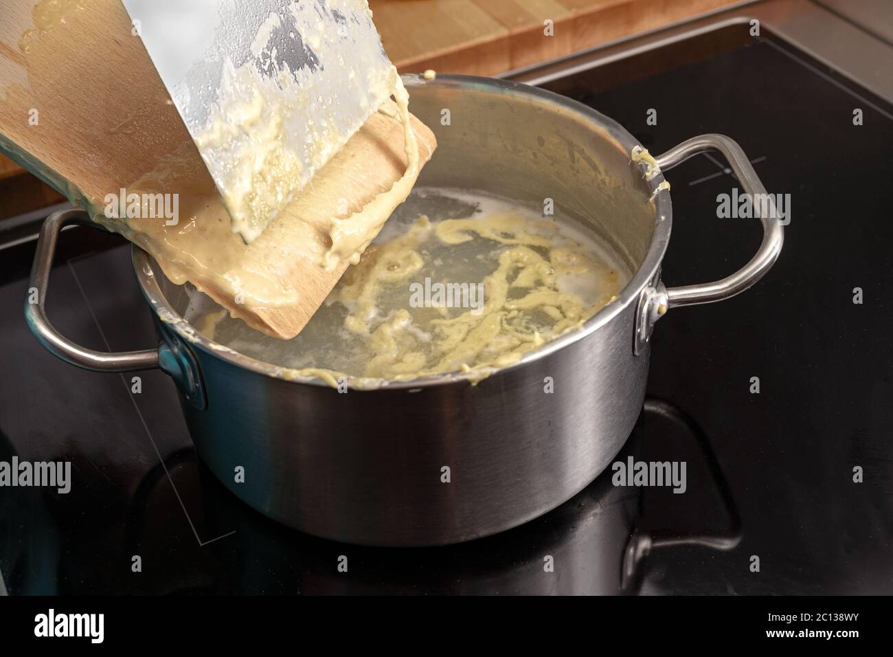 Cooking homemade spaetzle, egg pasta dough is scrapped from a wooden board into a pot with boiling water, typical dish in Schwaben, southern Germany a Stock Photo