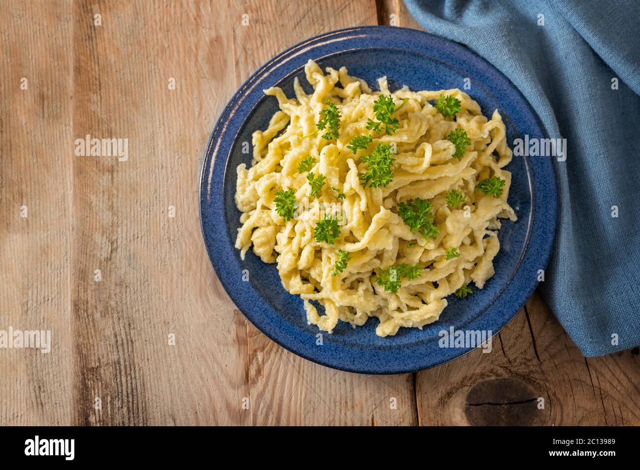 Spaetzle, homemade egg noodles served with parsley garnish on a blue plate and a rustic wooden table with copy space, traditional dish in Schwaben, so Stock Photo