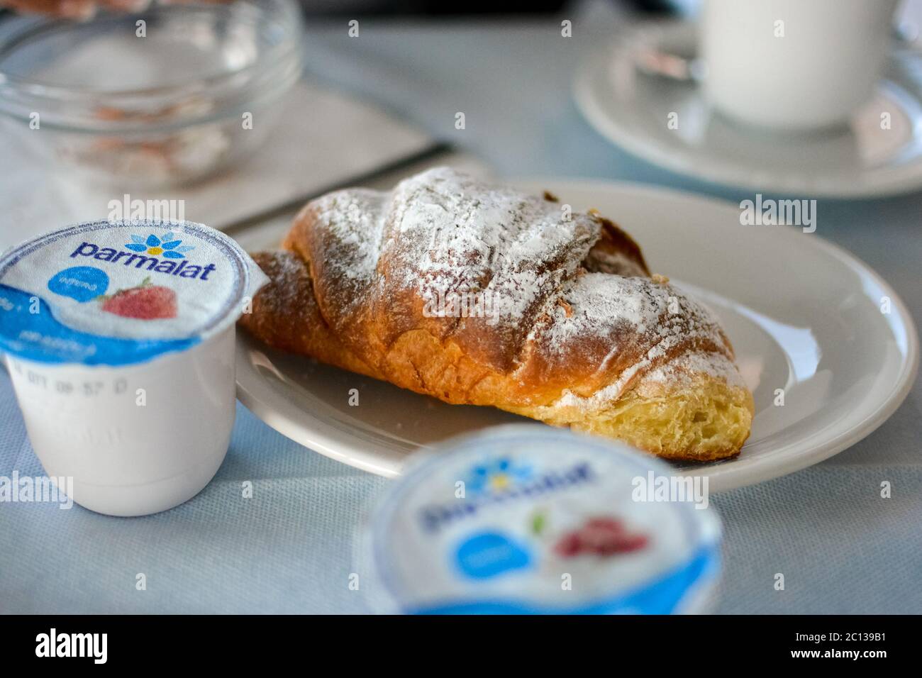 A continental breakfast in Italy featuring a croissant with powdered sugar and yogurt in a cap. Stock Photo