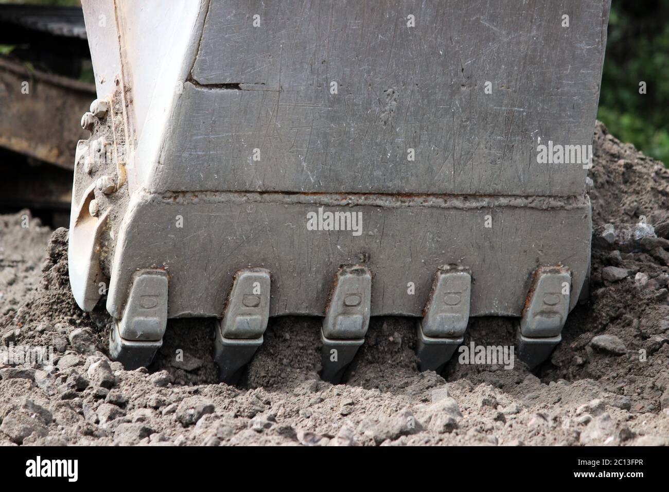 Excavator bucket digging a trench at the side of the road for its expansion. Stock Photo