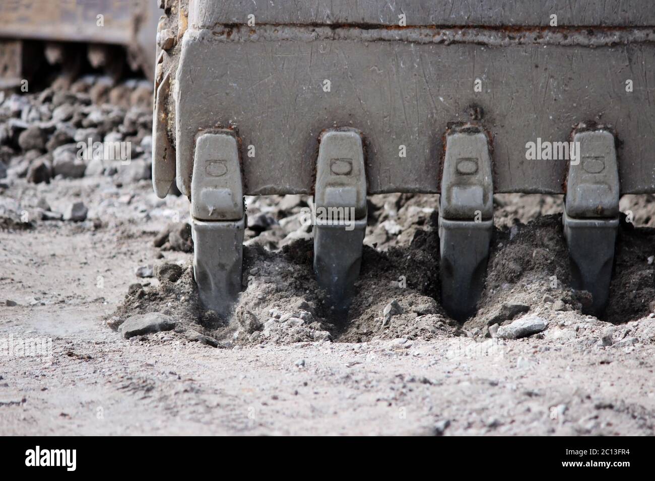 Excavator bucket digging a trench at the side of the road for its expansion. Stock Photo