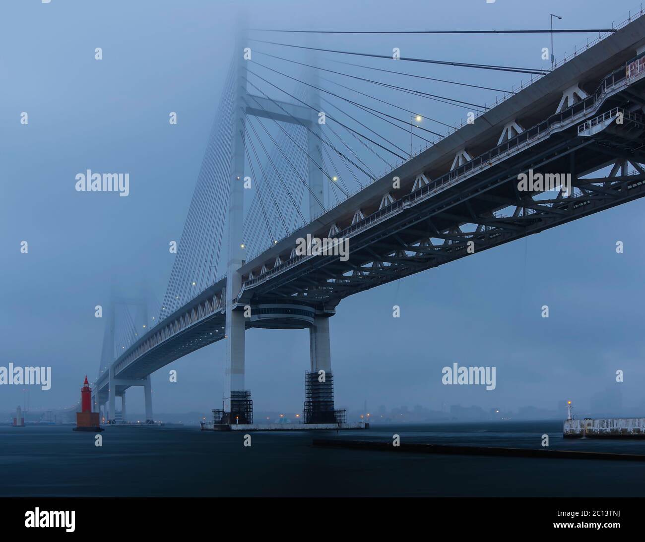 View of Yokohama Bay Bridge from Daikoku Pier West Park during the blue hour before sunrise under rainy and cloudy skies. Stock Photo