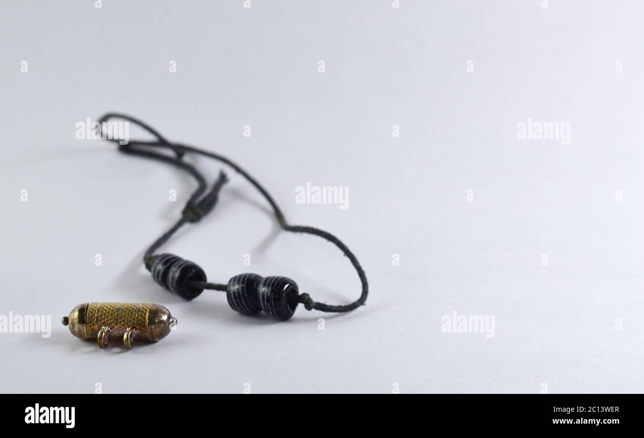 old pendant and beads on a black thread against a white background. Culturally used by Indian mothers to tie around new born child's waist. Stock Photo