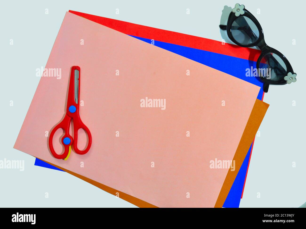 colour papers, scissors and specs on a white surface indicating a kid's activity desk Stock Photo