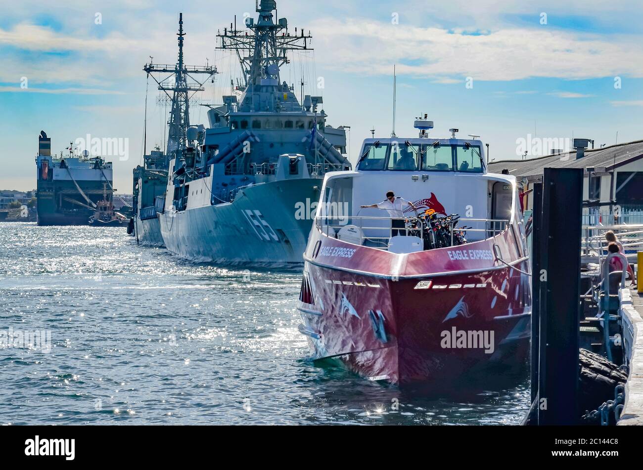 Moored in front of the Australian navy frigate HMAS Ballarat, a Rottnest Express ferry in Perth is prepared for its next journey to Rottnest Island Stock Photo