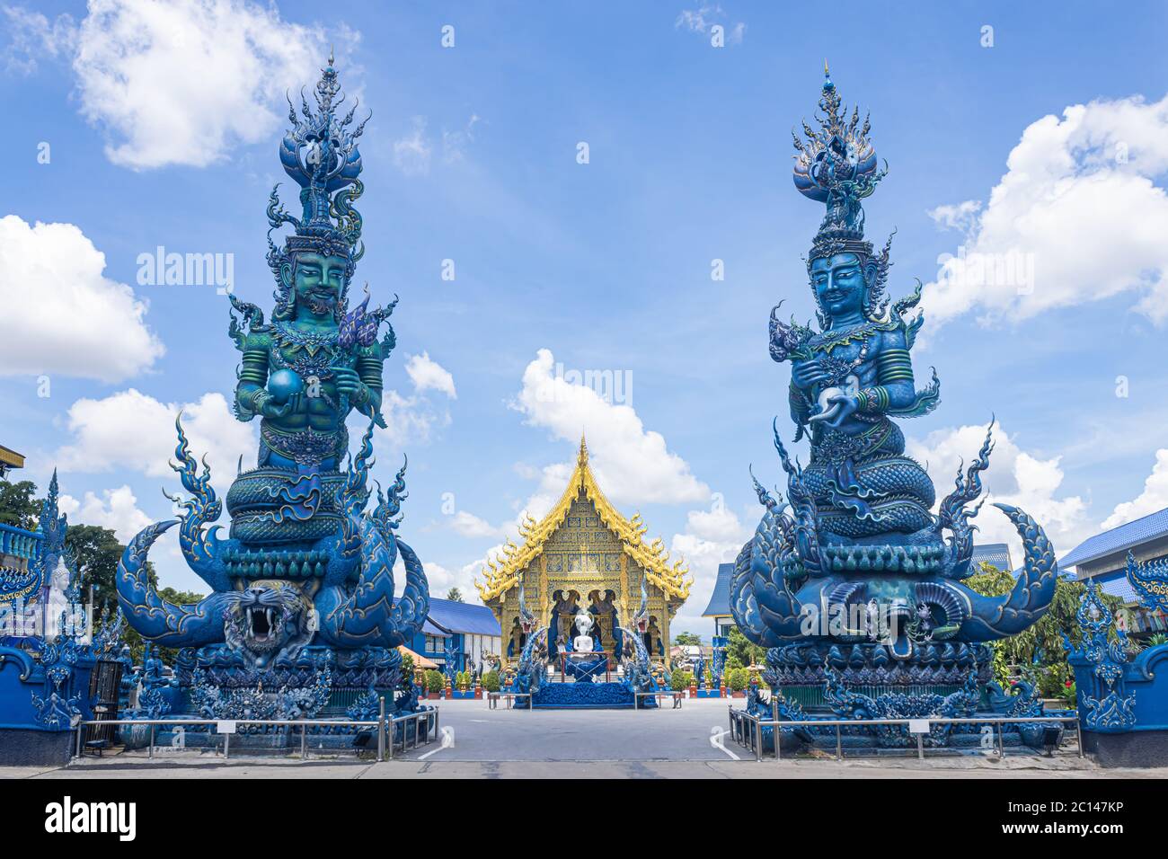 Chiangrai, Thailand - June 7, 2020: Green God and Blue God Hold Lotus and Yellow Blue Thai Church on Blue Sky Background in Wat Rong Suea Ten Temple Stock Photo