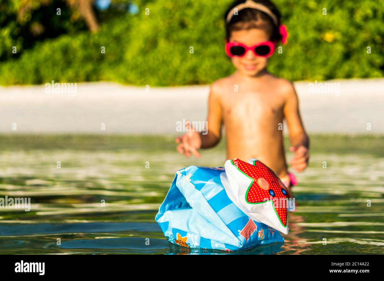 Little girl in greenish water on beach with tropical flora in the