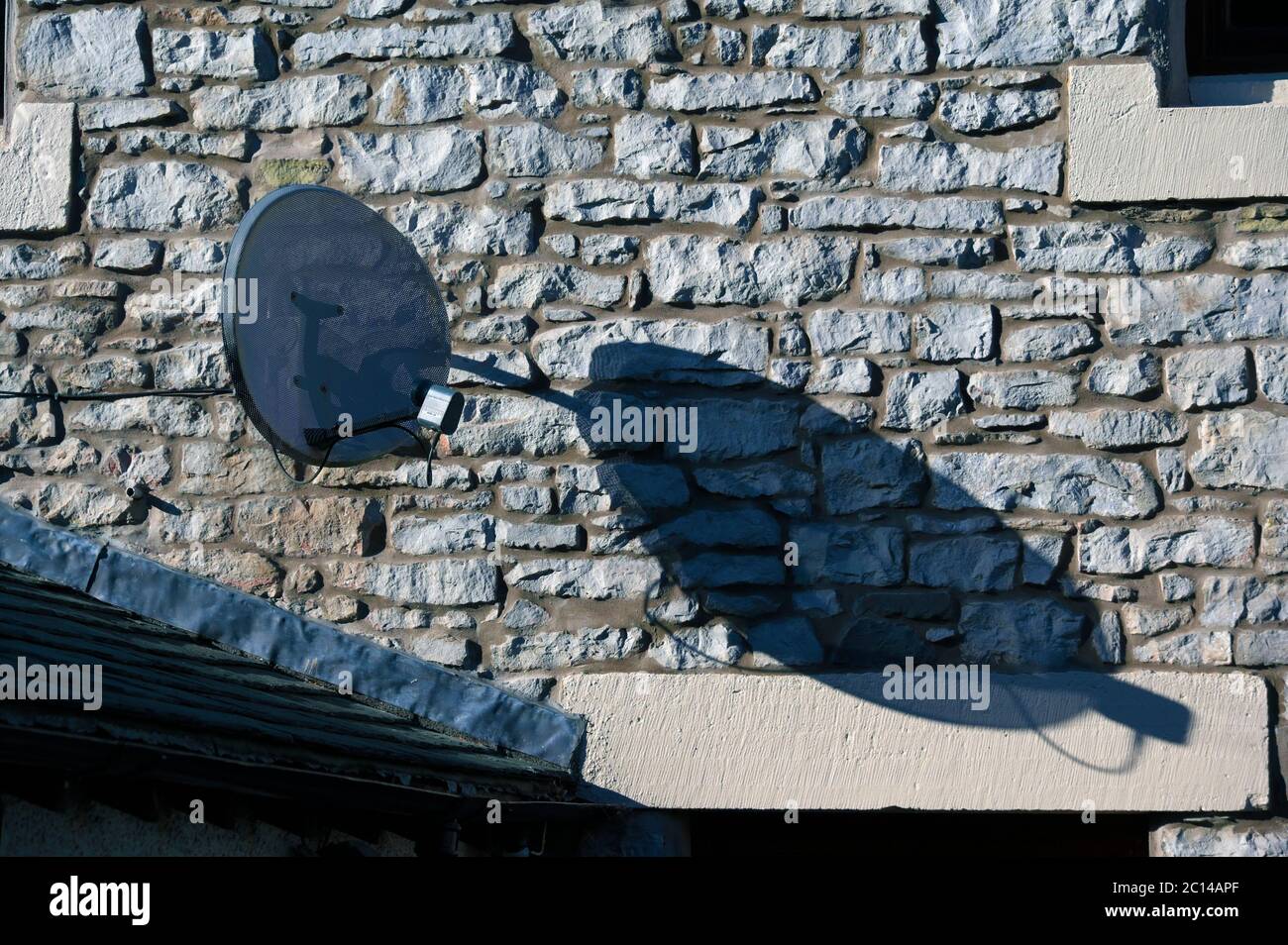 Satellite Dish on stone wall of house. Queen's Road, Fellside, Kendal, Cumbria, England, United Kingdom, Europe. Stock Photo