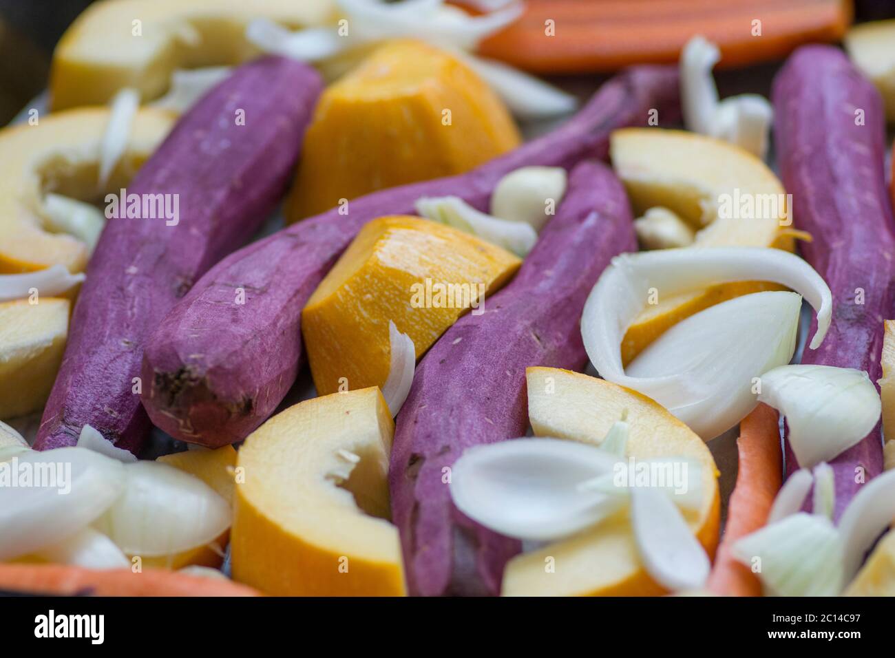 Colorful mix of root vegetables: carrots, yellow pumpkin, purple sweet potatoes, onions and garlic. Stock Photo